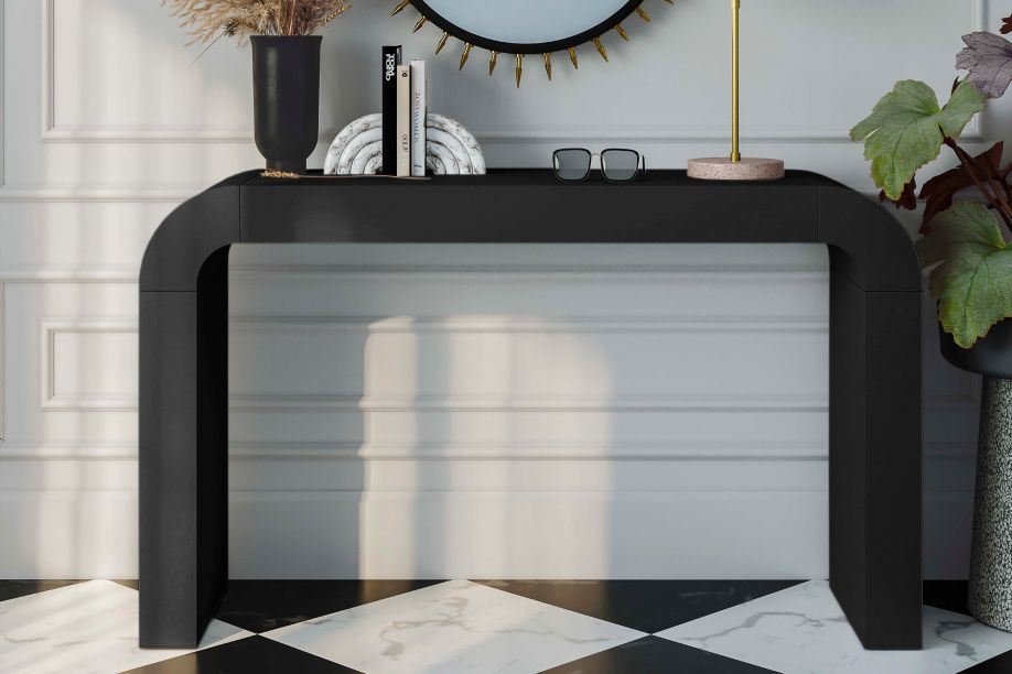 A black console table with decor on top, set against a white wall and checkered floor.
