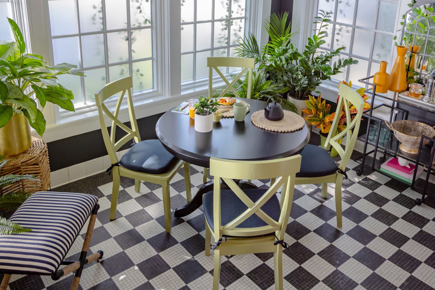 A sunroom with a round table, chairs, and plants. The floor is checkered.
