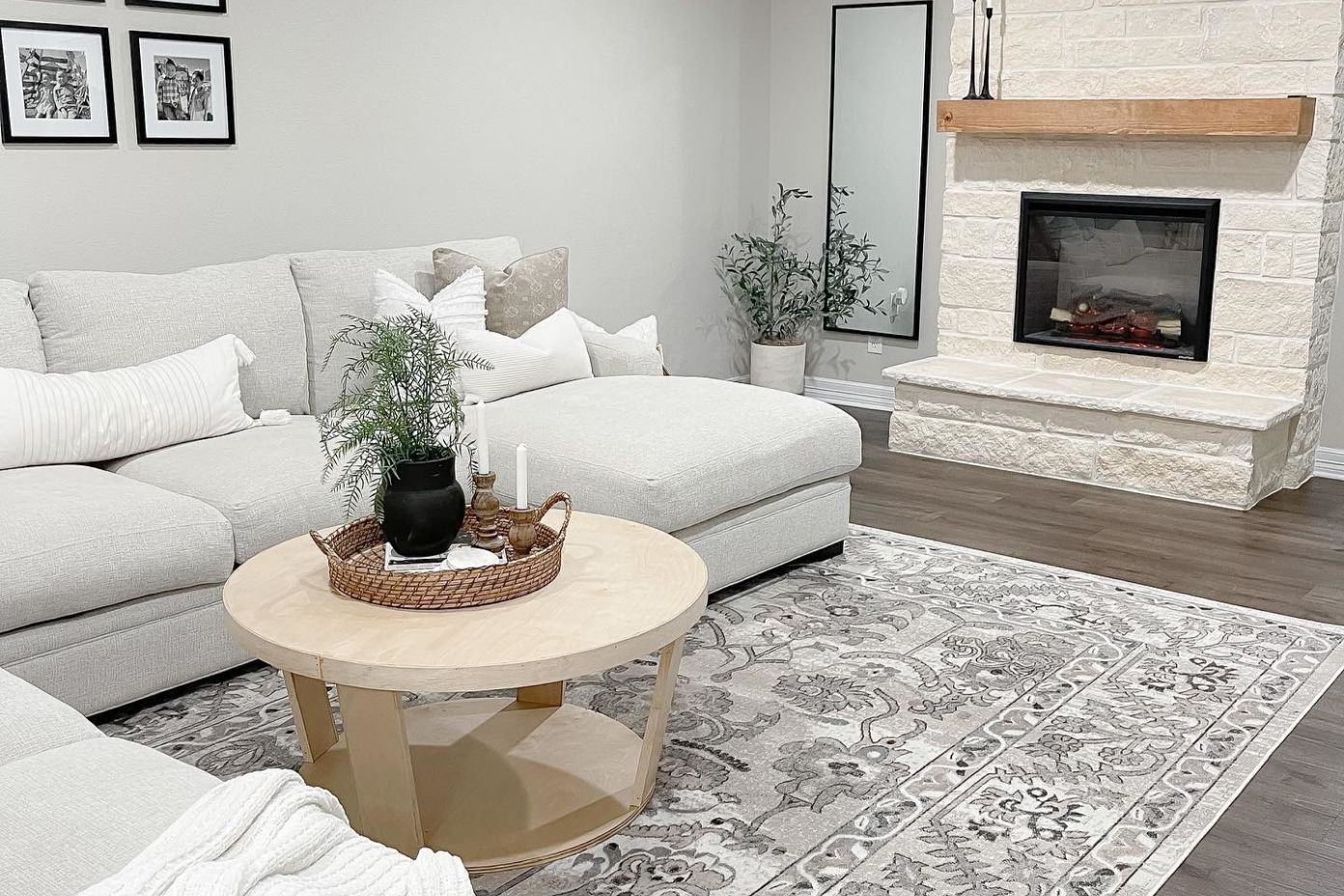 A living room with a light gray sectional sofa, a round coffee table, and a stone fireplace.
