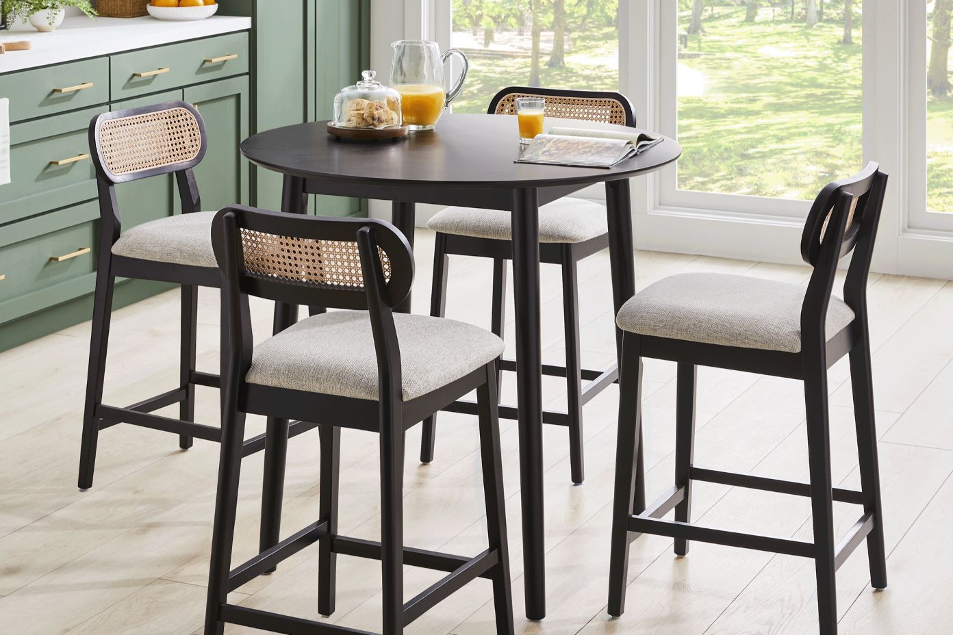 A black round kitchen table with four black bar stools with woven backs and light gray seats.
