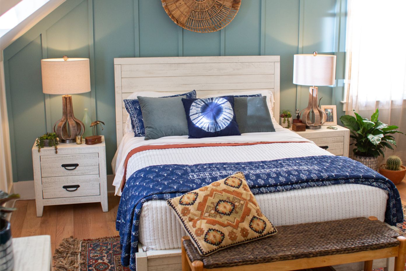 A bedroom with a white bed, blue bedding, and a patterned pillow. Two nightstands with lamps flank the bed.
