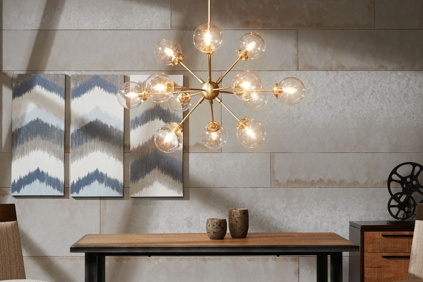 A modern dining room with a gold chandelier, wooden table, and artwork.
