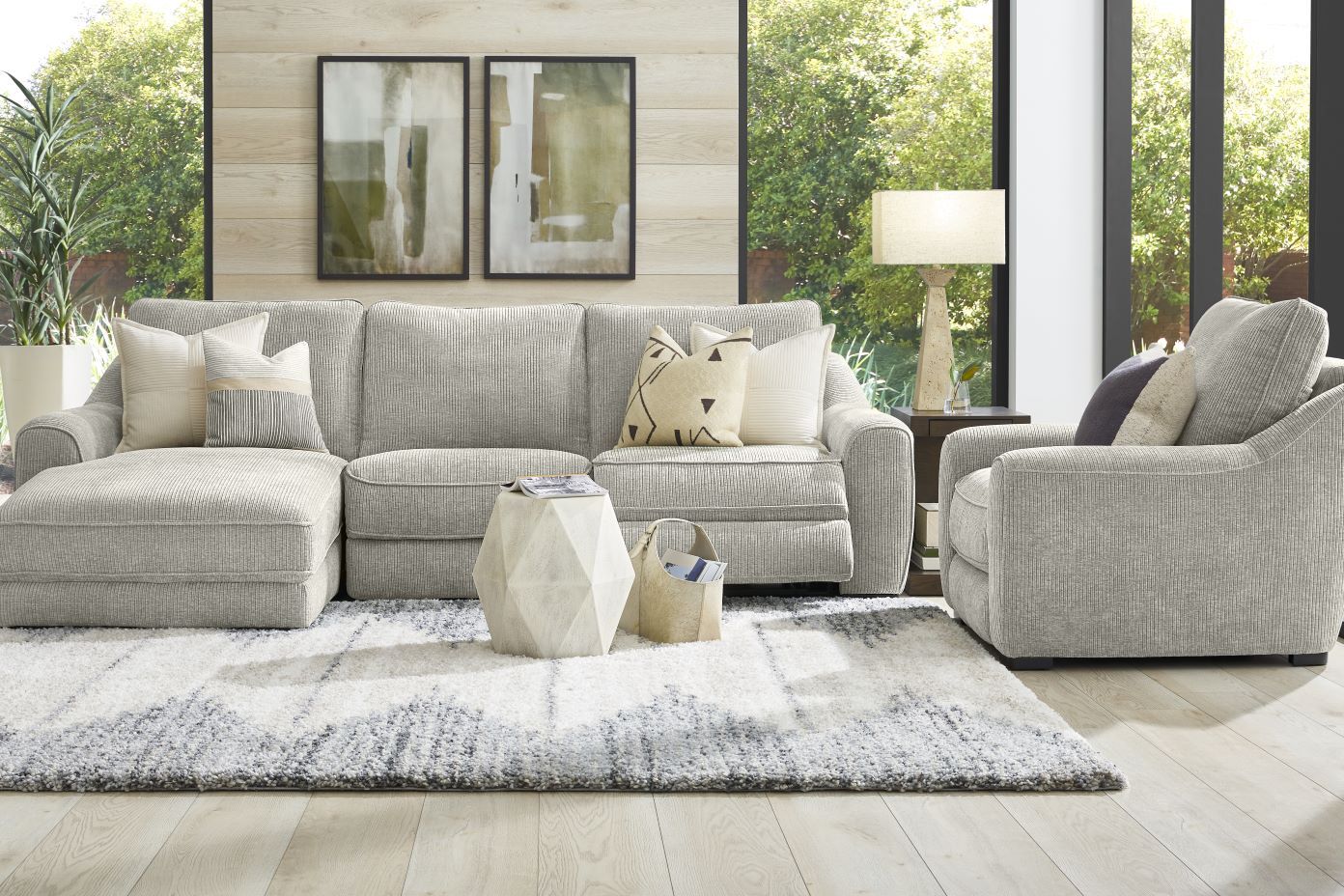 Gray sectional sofa and armchair with decorative pillows, rug, and side table.
