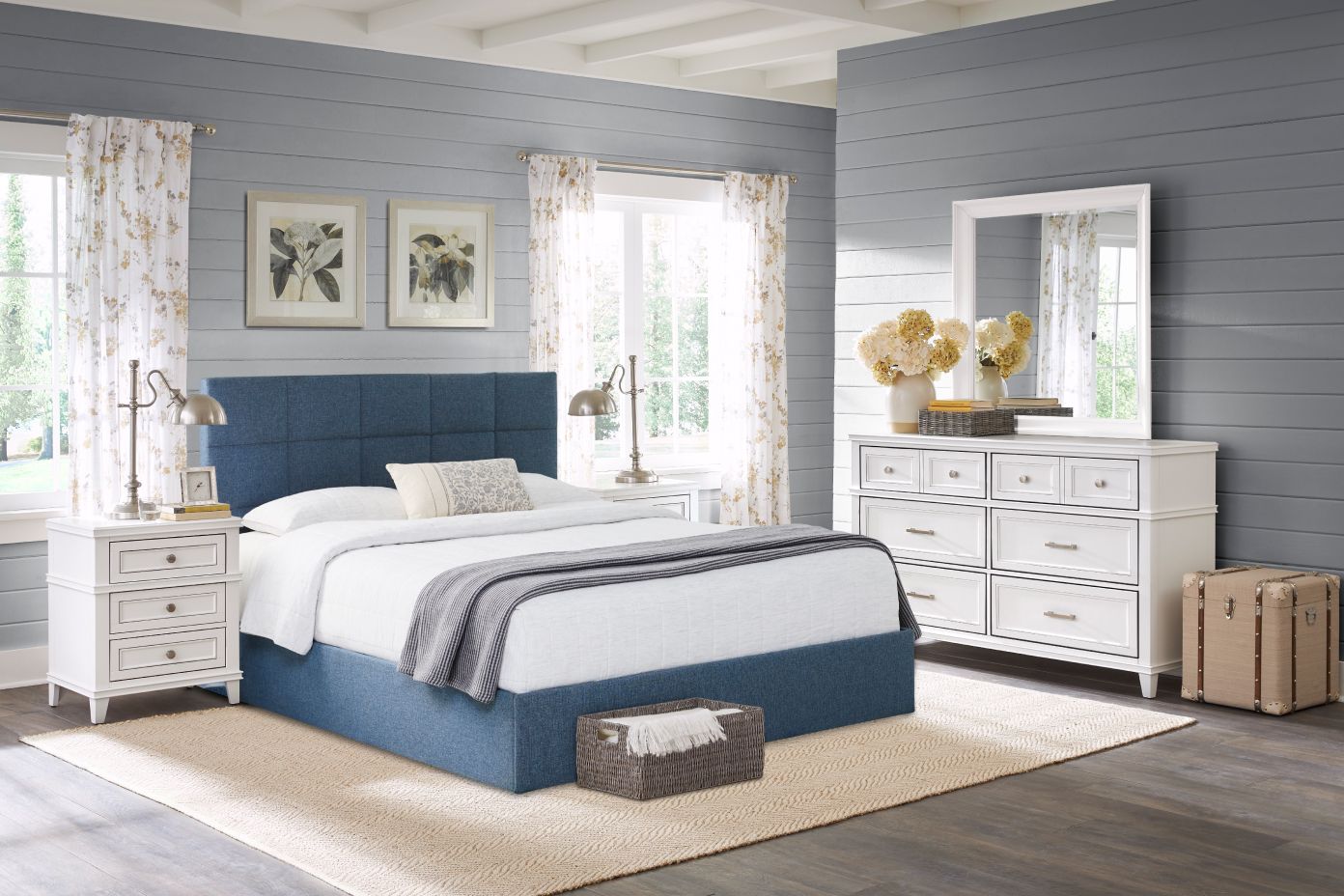 Bedroom with blue bed, white dresser, and floral curtains.
