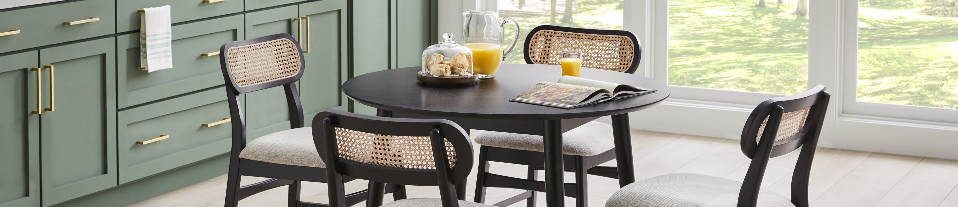 A round black dining table with four chairs, a glass of juice, and a book.