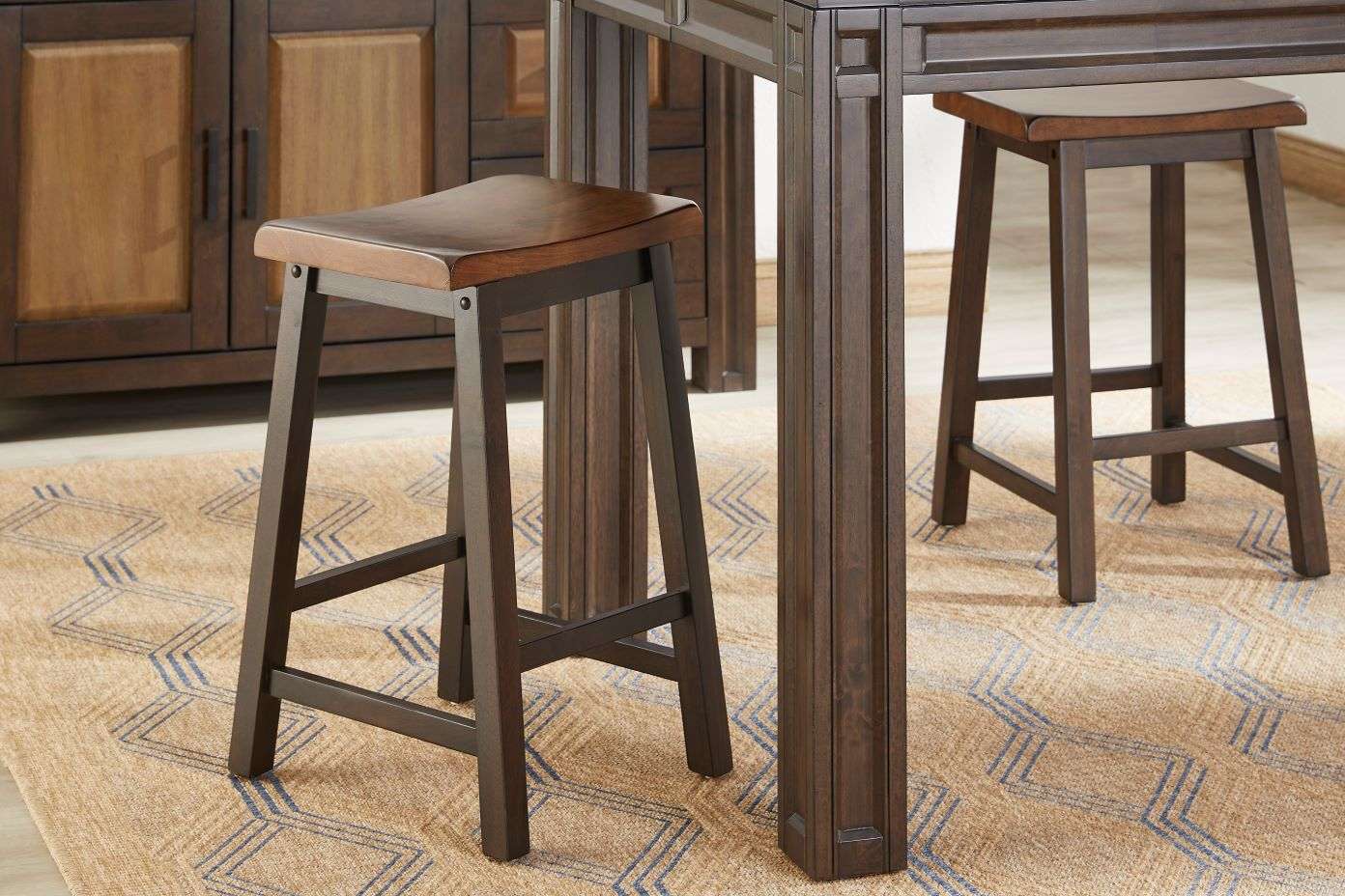 Two brown wooden bar stools with a dark brown table and a patterned rug.
