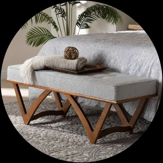 A gray upholstered bench with wooden legs, placed at the foot of a bed.
