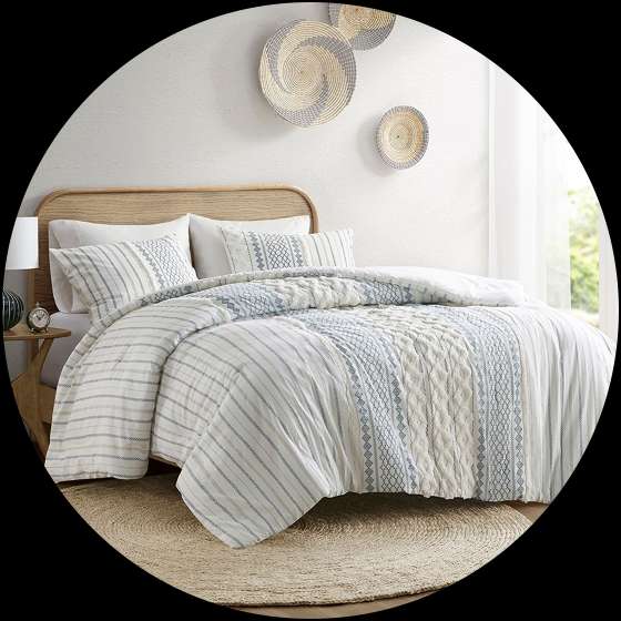 A bed with a white and blue patterned comforter and pillows, with a round jute rug.
