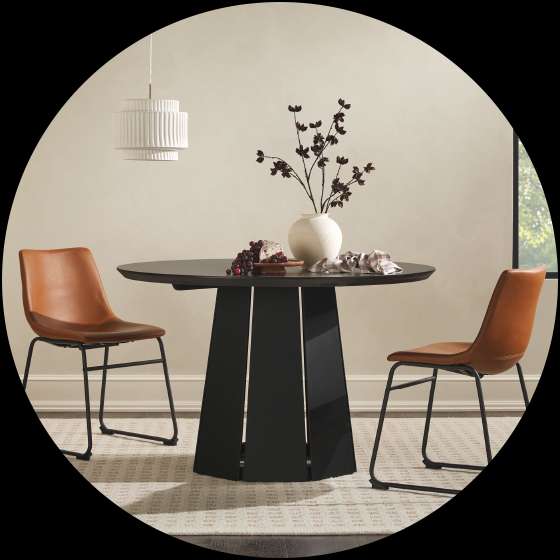 A round black dining table with two brown leather chairs.
