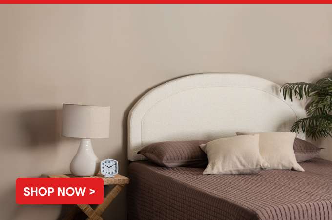 Shop Now > A bed with a white headboard, pillows, and a lamp on a side table.
