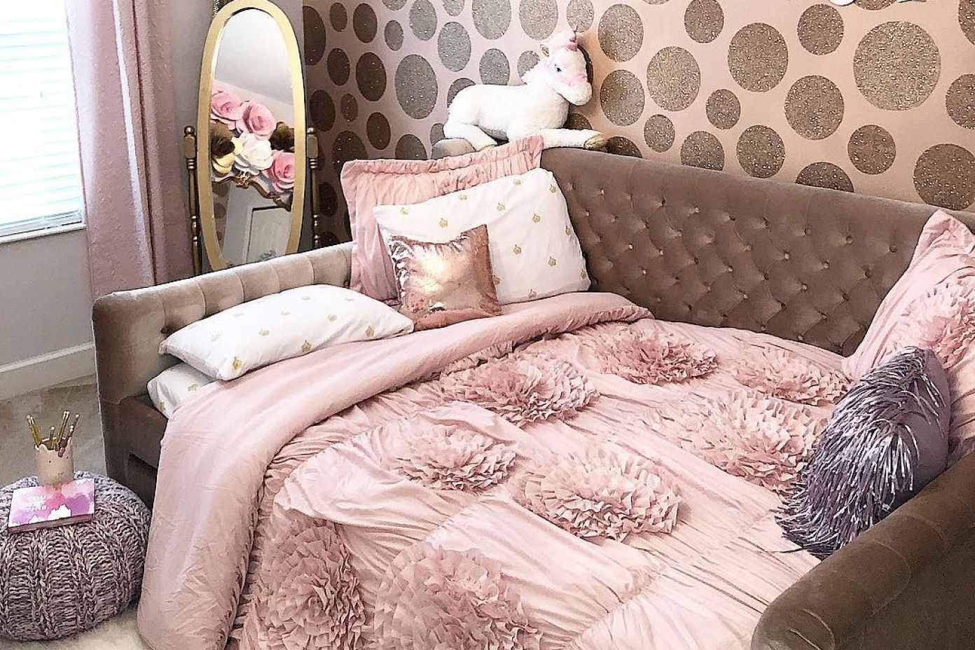 A pink bed with decorative pillows and a unicorn on the headboard.
