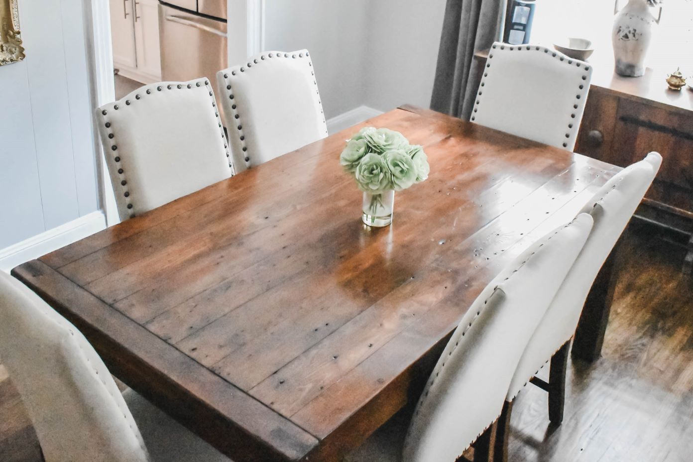 Wooden dining table with white upholstered chairs and a vase of flowers.
