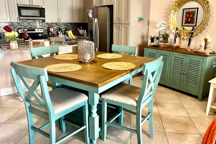 A dining room with a square wooden table and four teal chairs. A green cabinet is in the background.
