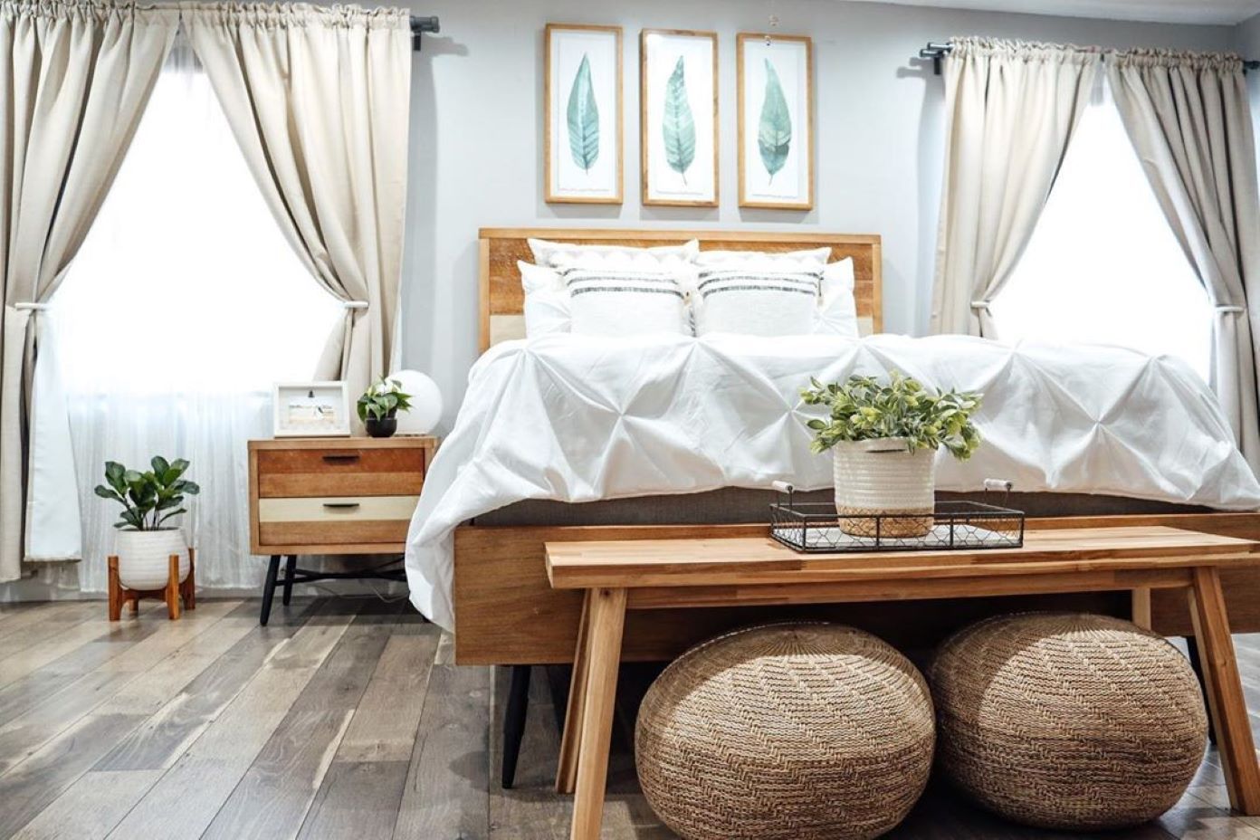 Bedroom with a wooden bed, white bedding, and a wooden bench with two woven poufs.
