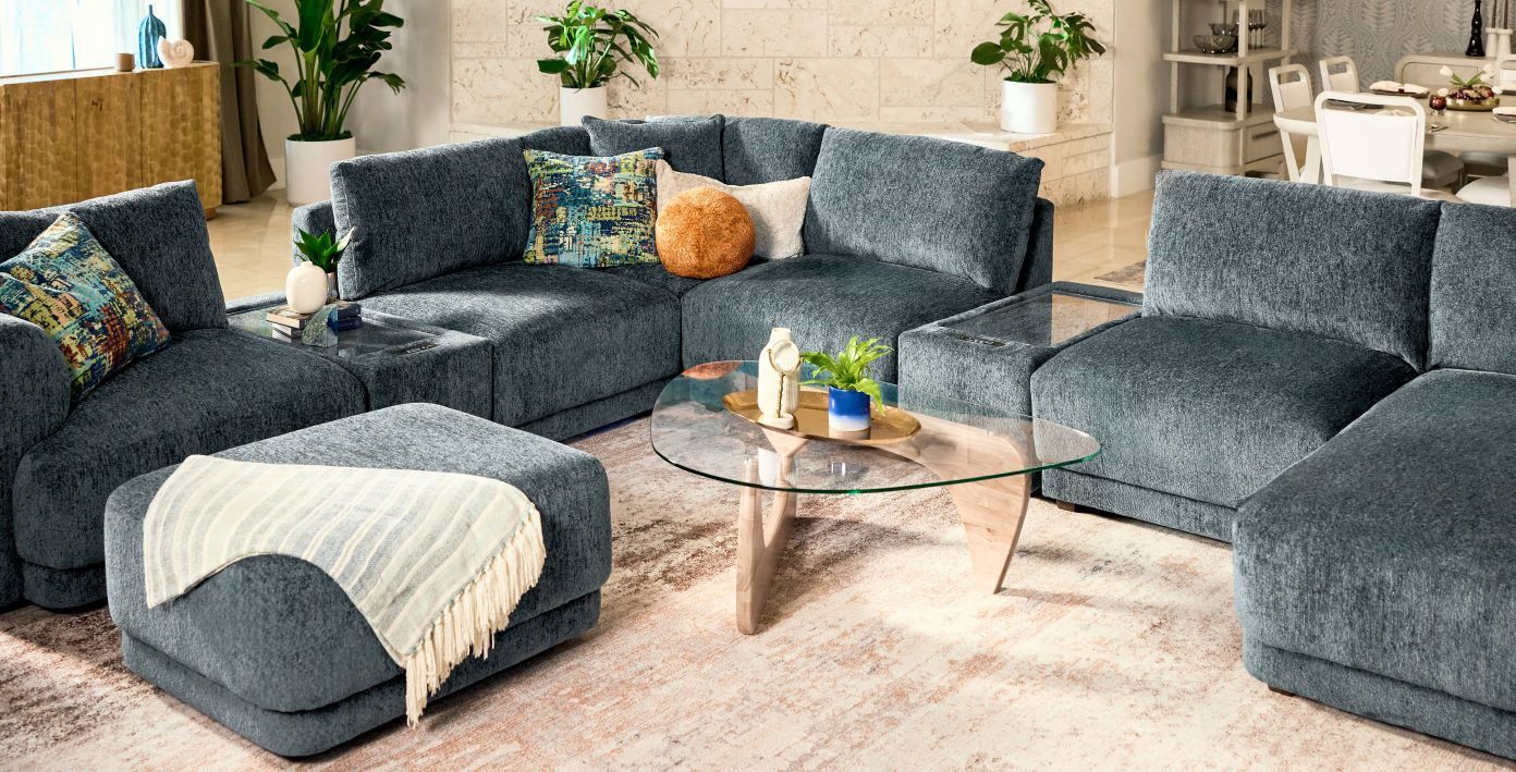 A sectional sofa with an ottoman and a glass coffee table.
