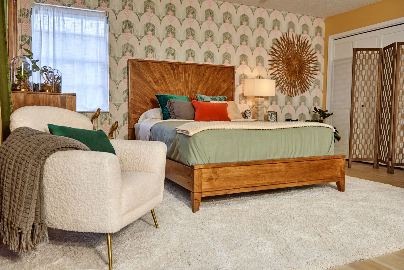 Bedroom with a wooden bed, white armchair, and patterned wallpaper.
