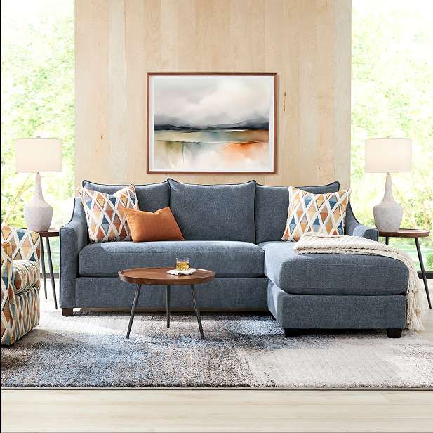 A blue sectional sofa with decorative pillows, a round coffee table, and a landscape painting.
