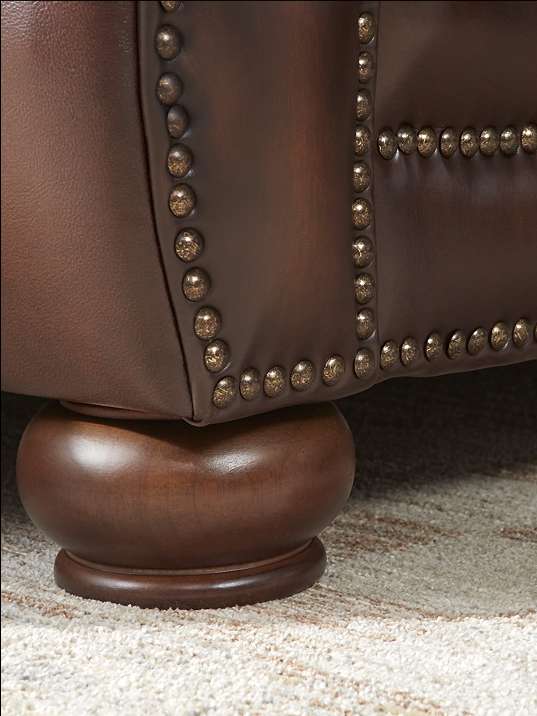 Brown leather armchair with brass nailhead trim and a wooden bun foot.
