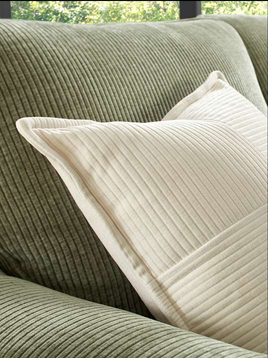 Close-up of a white corduroy pillow on a green corduroy couch.
