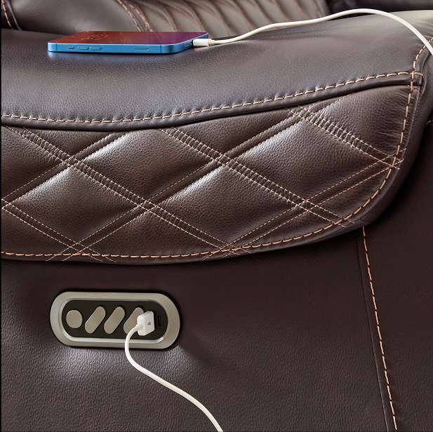 Close-up of a brown leather recliner with a phone charging.

