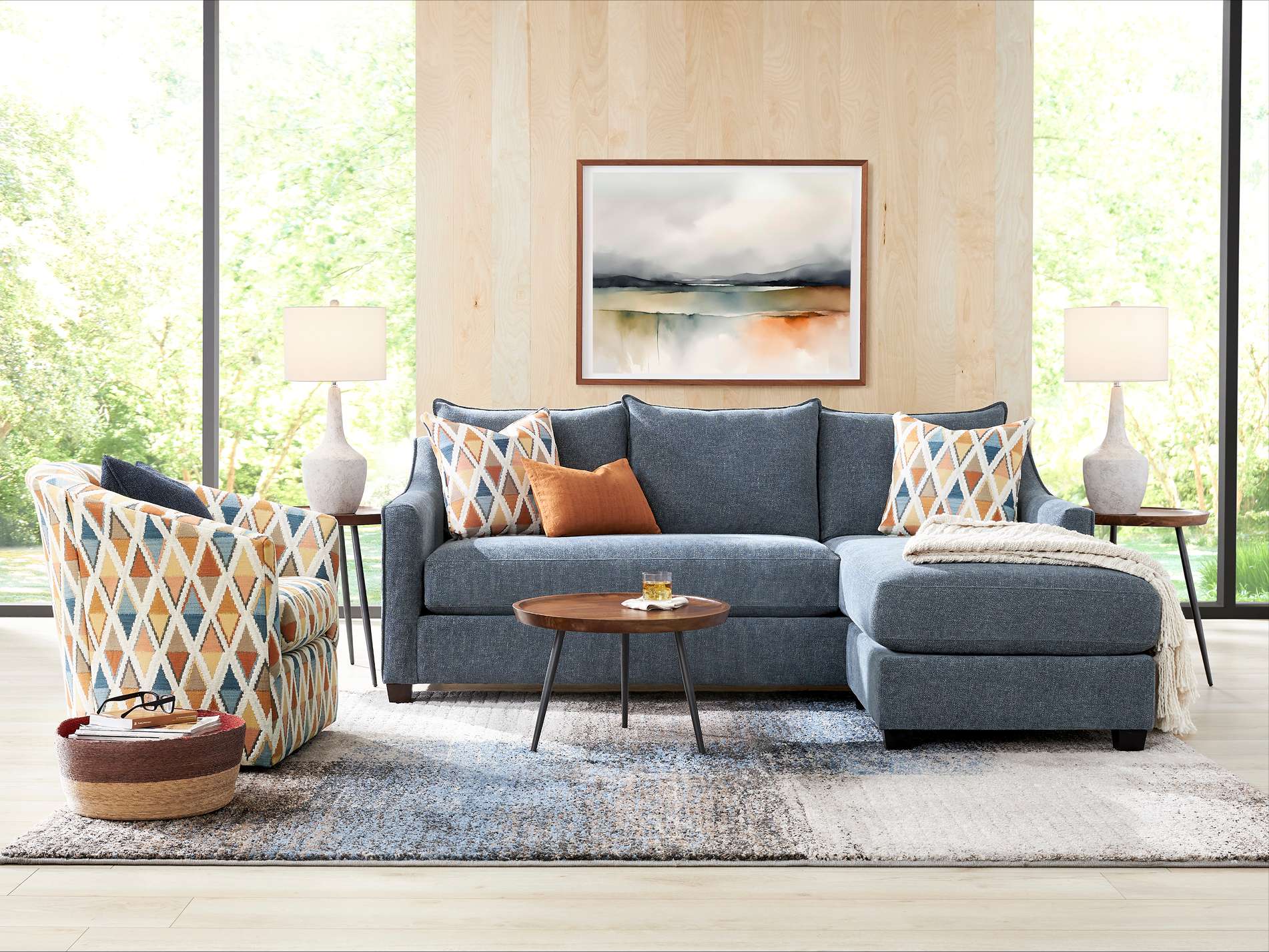 A living room with a blue sectional sofa, patterned armchair, and a round coffee table.
