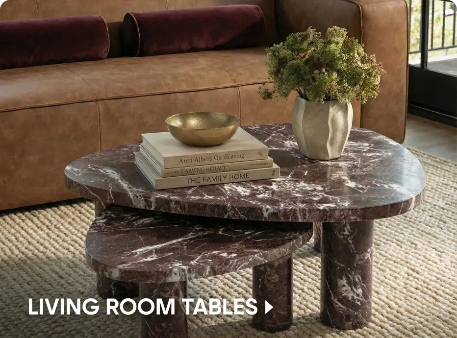 LIVING ROOM TABLES: A nested, dark red marble coffee table with a bowl, books, and a vase on top, set on a textured rug.