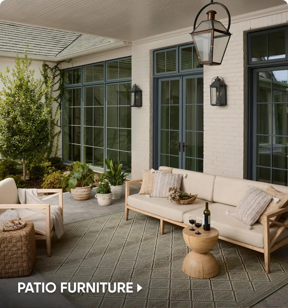 PATIO FURNITURE: A modern outdoor seating area with a beige sofa, armchair, and wooden side table on a patterned rug.