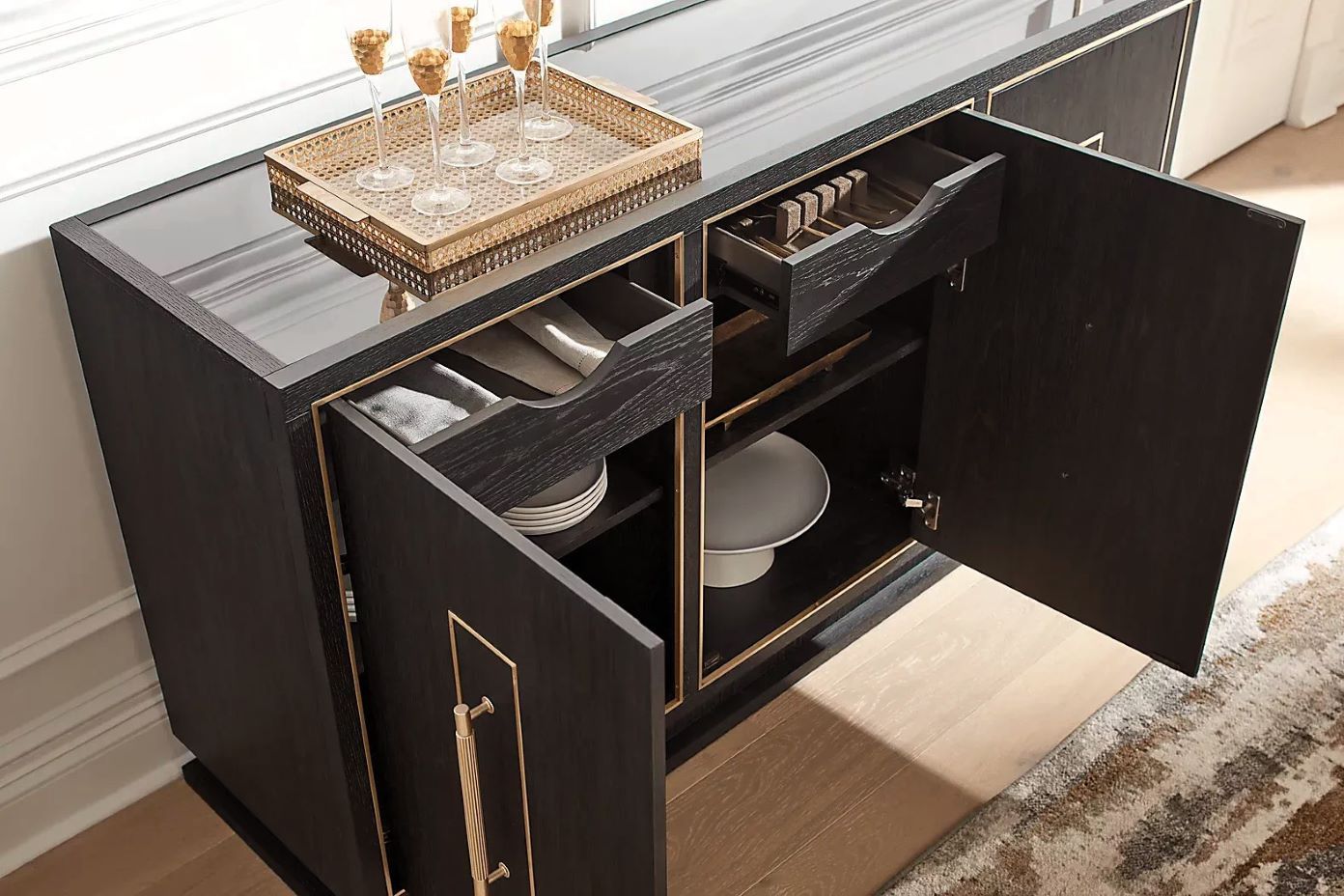 Black buffet with gold trim, open doors, and drawers. Champagne glasses and a tray are on top.
