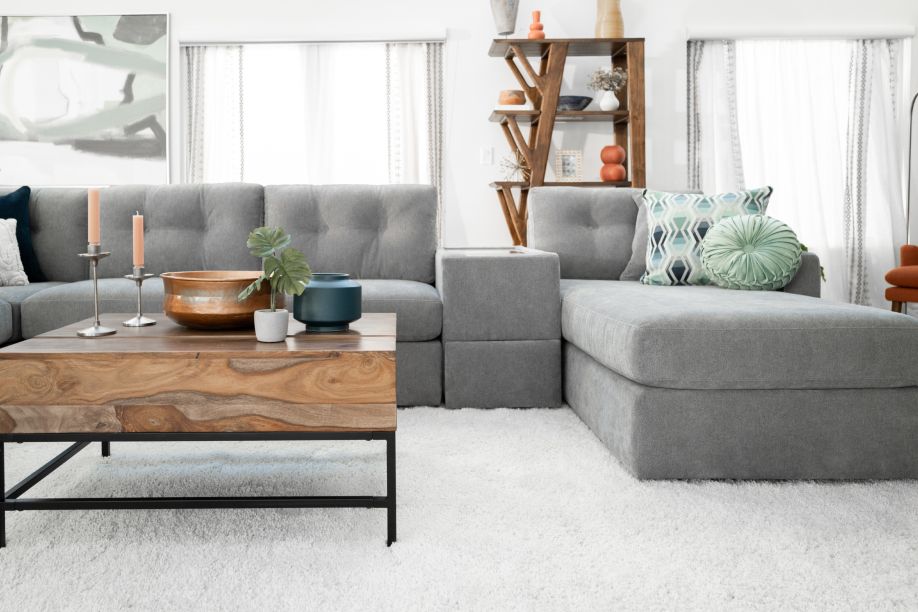 A gray sectional sofa with a wooden coffee table and a white shag rug.
