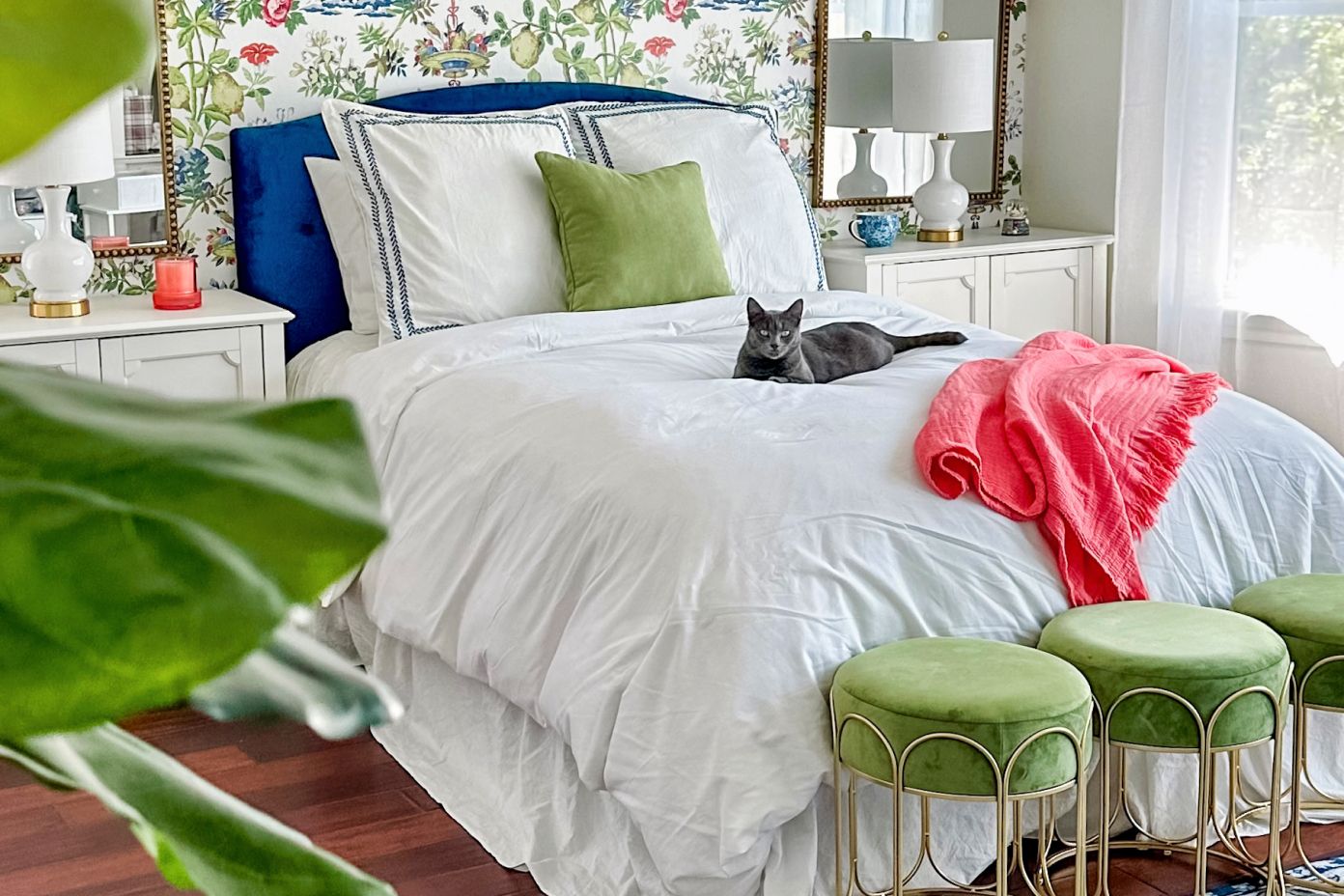 A bedroom with a bed, a cat, and green velvet stools.

