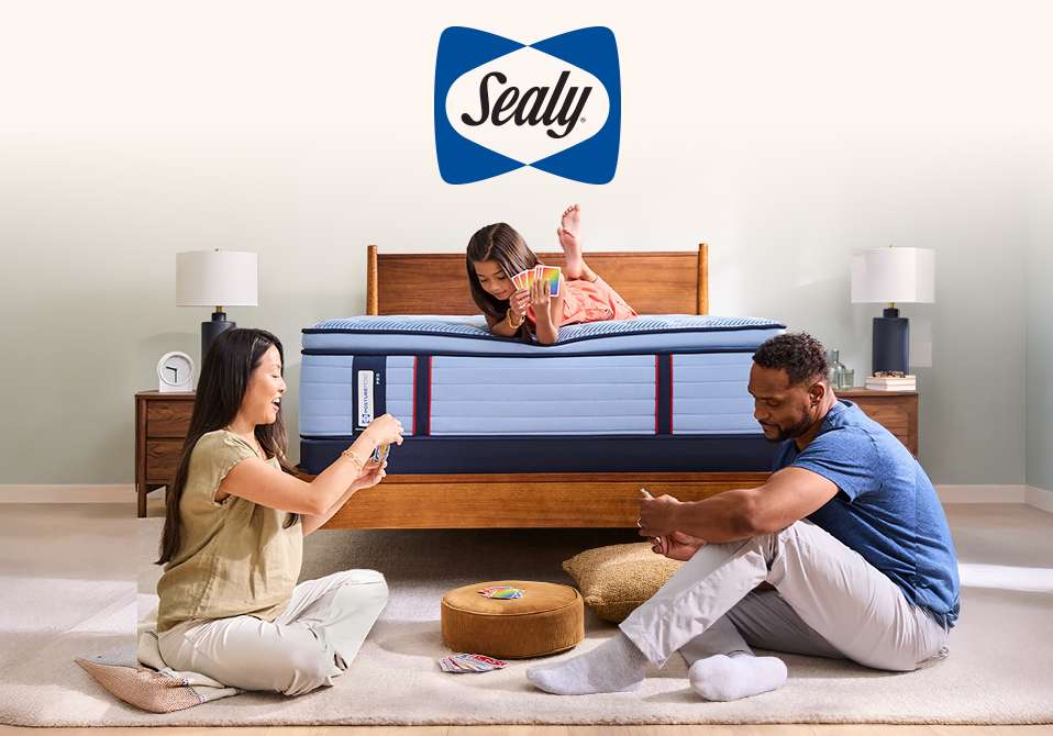 Sealy logo. A family playing cards on a bed.
