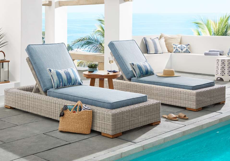 Two wicker chaise lounges with blue cushions by a pool.
