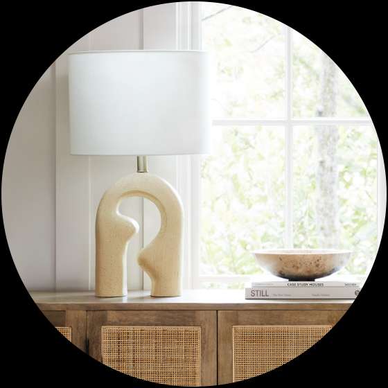 A cream-colored lamp with a unique base sits on a wooden cabinet.
