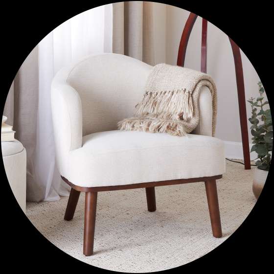 Cream-colored armchair with a blanket draped over it, set on a textured rug.
