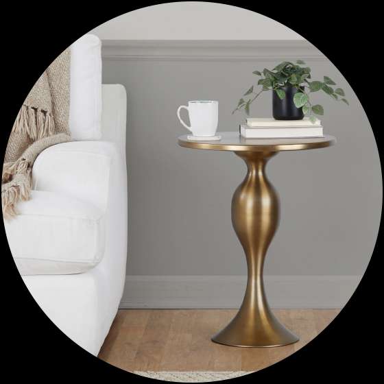A gold side table with a plant, books, and a mug next to a white couch.
