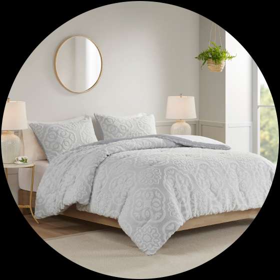 A bed with a white patterned comforter, pillows, and a round mirror on the wall.
