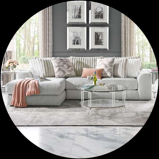 A modern living room with a light gray sectional sofa, a glass coffee table, and framed art.
