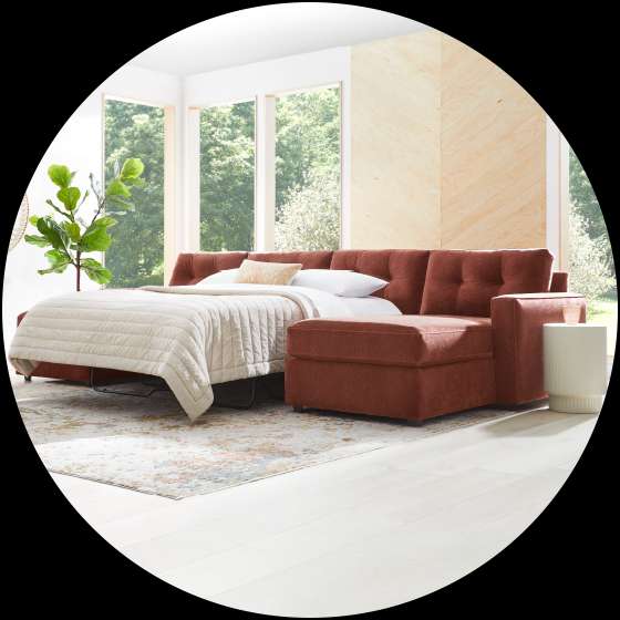 A rust-colored sectional sofa with a pull-out bed in a bright room.

