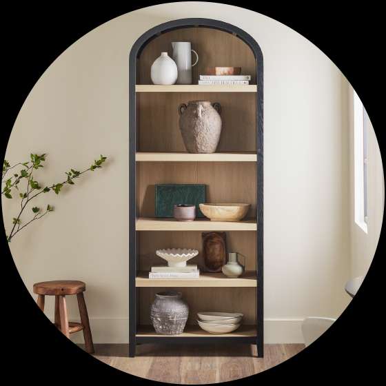 A tall, arched bookcase with various decorative items on the shelves.

