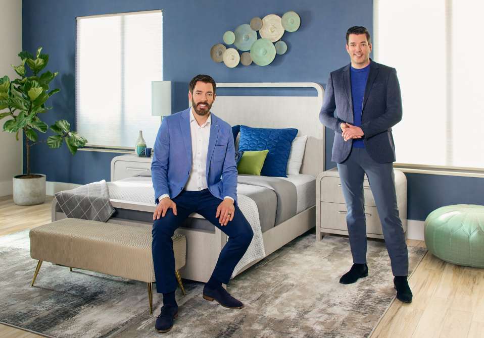 Two men in suits posing in a bedroom.

