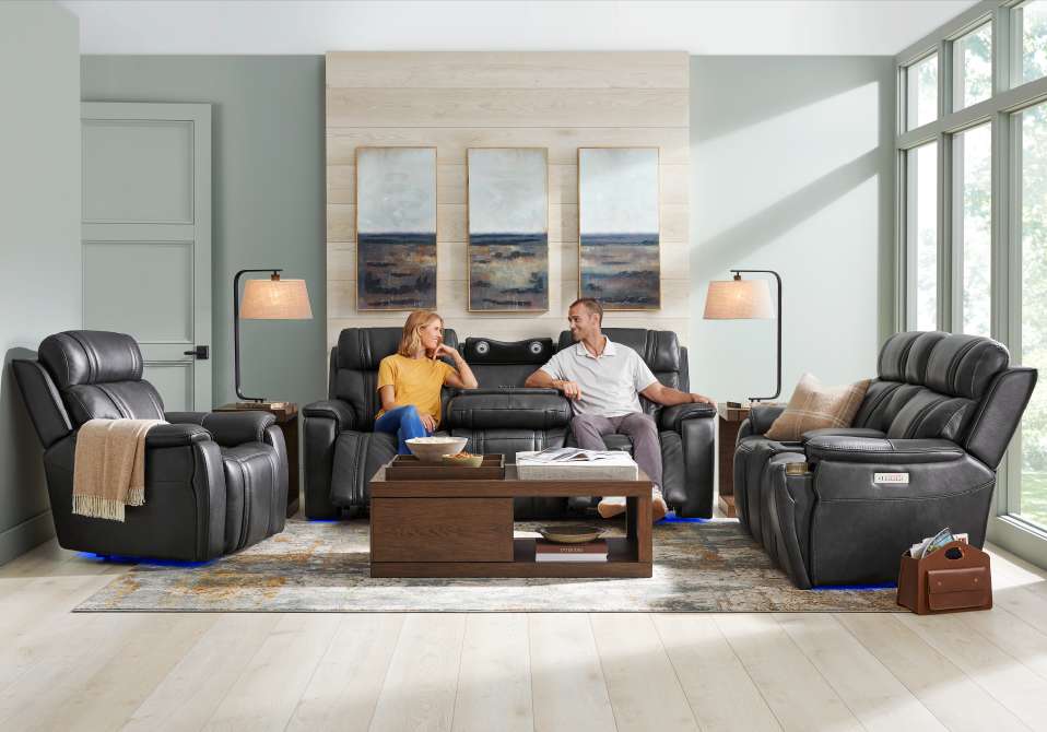 A living room with black leather recliners, a couple, and a coffee table.

