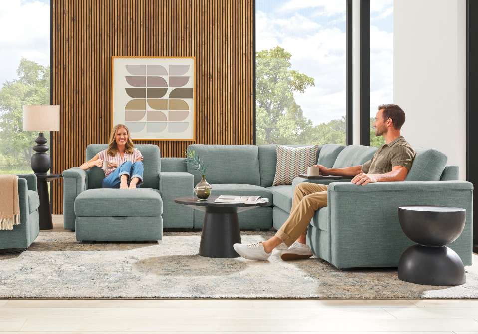 A living room with a sectional sofa, two people, and a coffee table.
