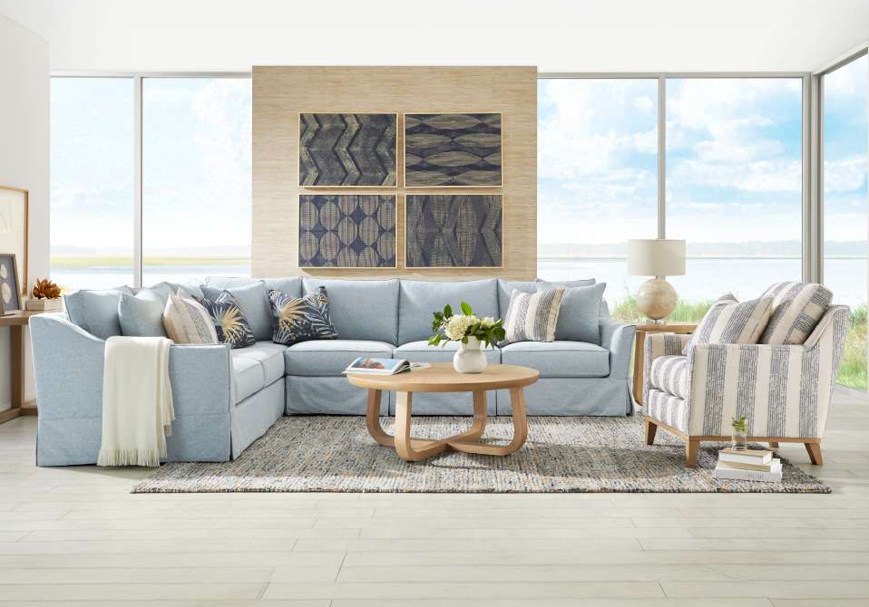 A light blue sectional sofa with patterned throw pillows, a striped armchair, and a wooden coffee table.
