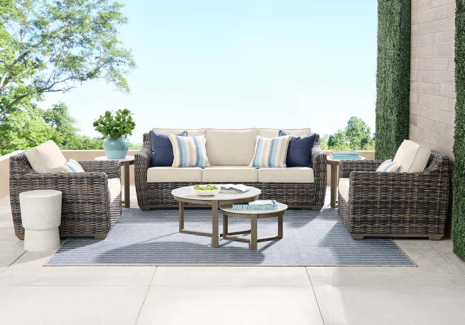 Outdoor patio furniture set with a sofa, two armchairs, and two coffee tables on a blue rug.
