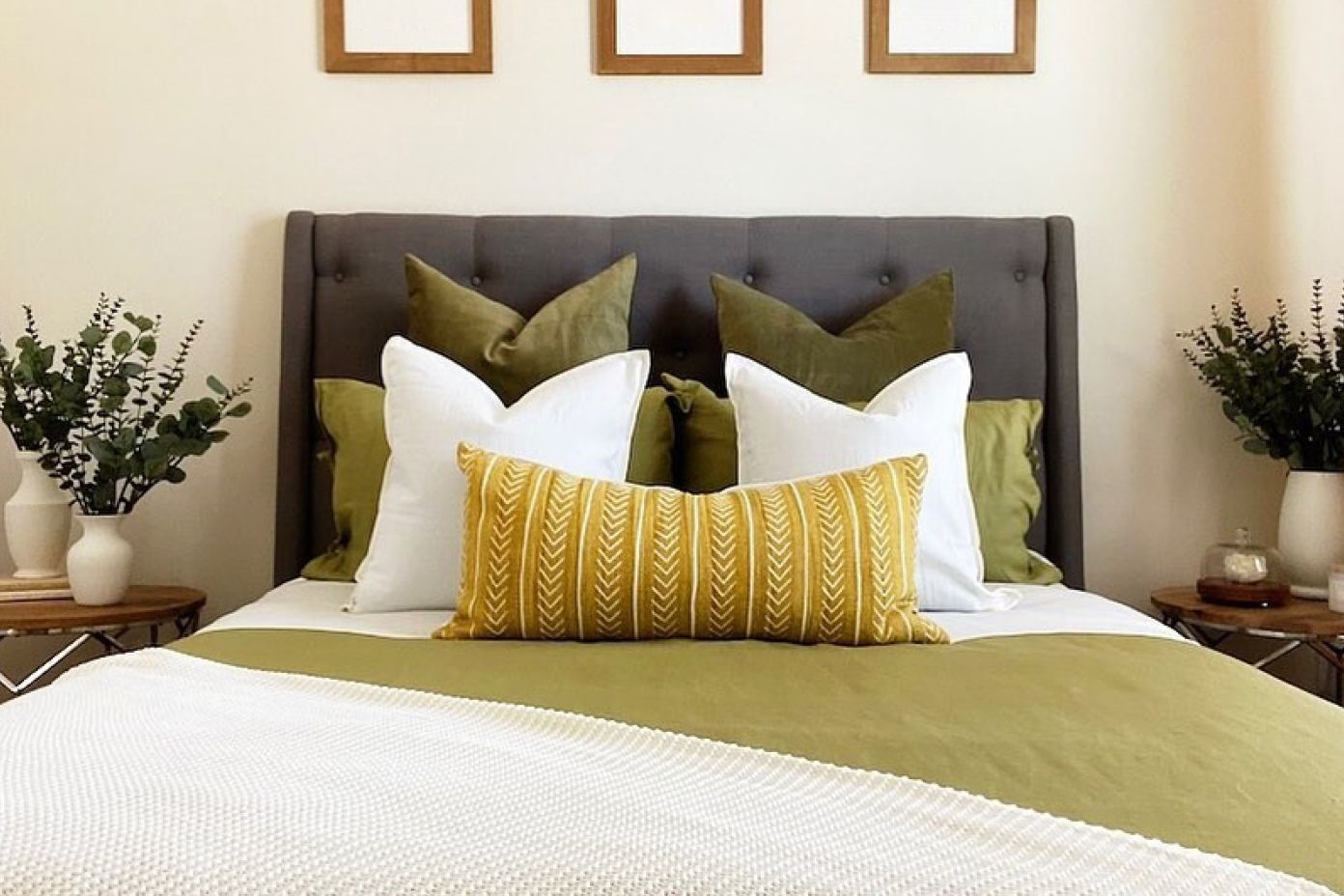 A bed with a gray headboard, green bedding, white pillows, and a yellow patterned pillow.
