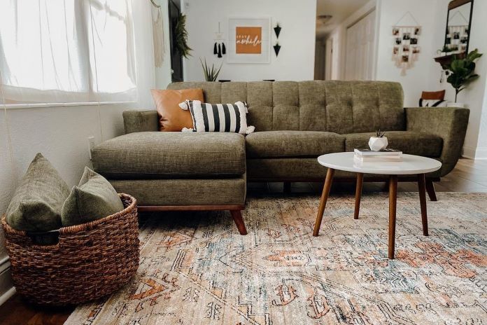 A living room with a green sectional sofa, a white coffee table, and a patterned rug.

