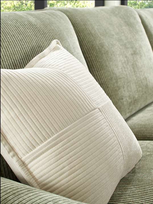 Close-up of a cream-colored pillow on a green corduroy couch.
