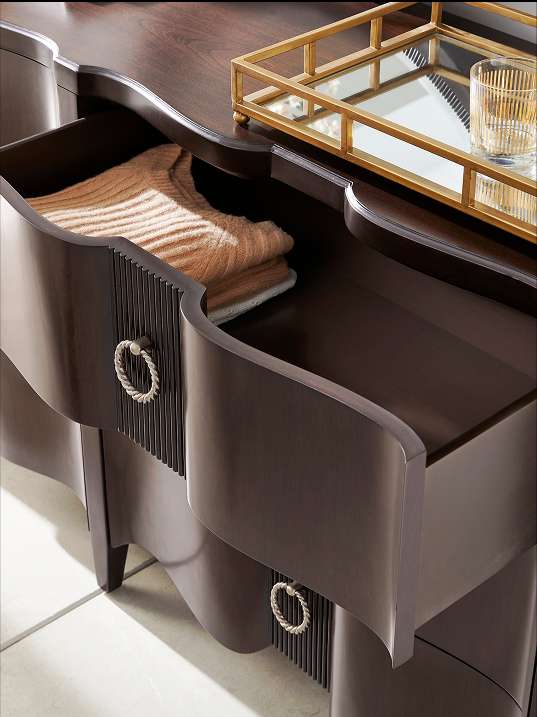 Dark brown dresser with open drawers, one containing folded sweaters. A gold tray and glass sit on top.
