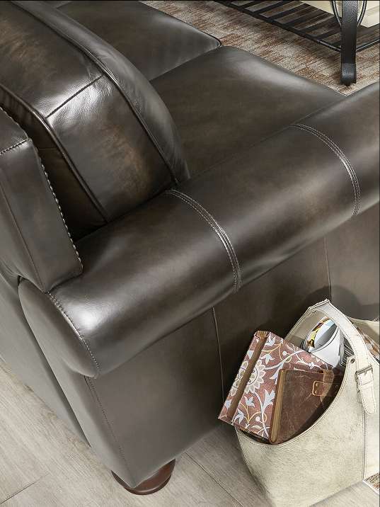 A close-up of a dark brown leather armchair with a magazine holder.
