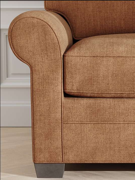 Close-up of a brown upholstered sofa with a rounded arm and a dark square leg.
